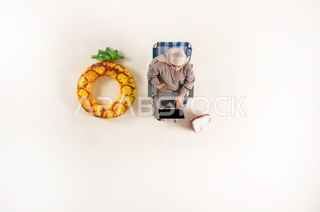 Integration and focus to accomplish tasks remotely, vertical upper portrait of an Arab Gulf Omani woman wearing hijab and abaya sitting on a chair working on a laptop, performing practical tasks and duties, Saudi woman using modern technological devices, white background