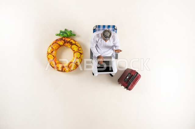 Taking advantage of advanced technology and techniques, vertical portrait of an Arab Gulf Omani man wearing a dishdasha and a kimono sitting on a sofa, working on a laptop, spending time with oneself, completing tasks remotely, white background