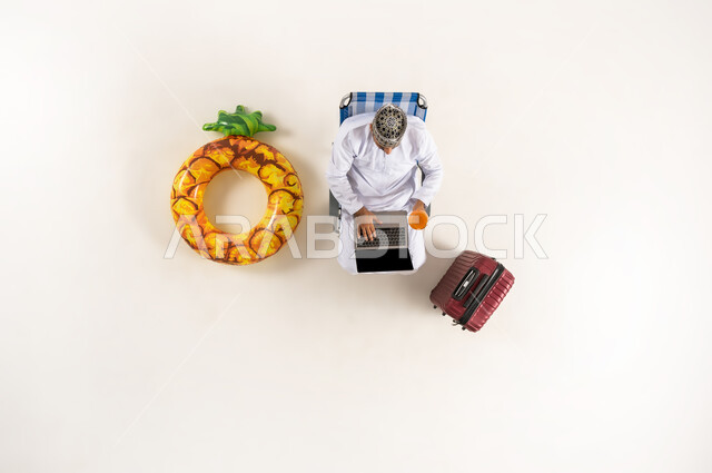 الجلوس و العمل على الحاسوب المحمول، الاستفادة من التكنولوجيا والتقنيات المتطورة، بورتريه عامودي علوي لرجل عربي خليجي عماني يرتدي الدشداشة والكمه، قضاء الوقت مع الذات، انجاز المهام عن بعد، خلفية بيضاء