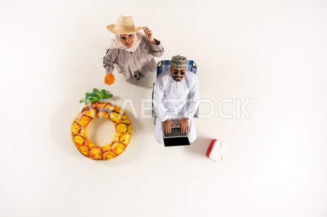 Spending fun recreational activities with wife, looking at camera with gestures of enthusiasm and joy, vertical overhead portrait of a Saudi Arabian Gulf couple wearing a dishdasha and a turban and wearing sunglasses working on a laptop, enjoying refreshing summer drinks, white background