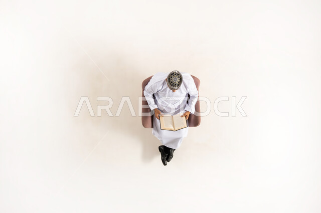أهمية المطالعة في المجتمع العماني, استغلال الوقت في التثقف، مفهوم التمعن والتركيز، قضاء الوقت بالقراءة والتعلم والثقافة ، بورتريه عامودي علوي لرجل عربي عماني خليجي يرتدي الدشداشة والكمه يجلس على كرسي مريح ويحمل بيديه كتاب، خلفية بيضاء