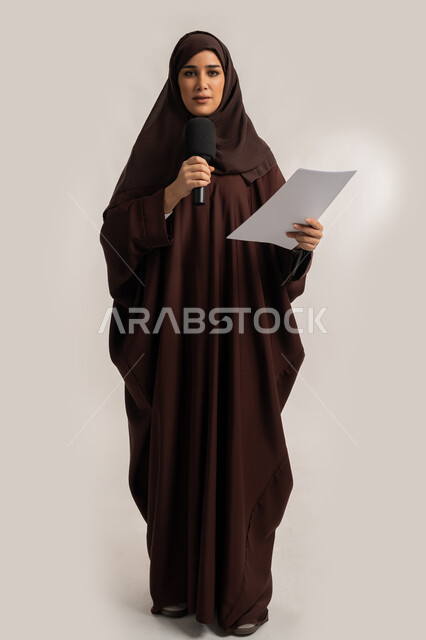 إقامة ورش العمل والدورات التدريبية، التواصل الفعال وتبادل الحوار والنقاش، إمرأة سعودية تقوم بالقراءة من الورقة، فن الالقاء والخطابة، بورتريه لشابة عربية خليجية اماراتية محجبة ترتدي العباءة تمسك مكبر الصوت تلقي الخطابات بإيماءات الثقة، الجسم بالطول الكامل، خلفية بيضاء