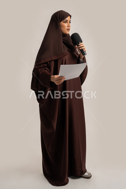 إقامة ورش العمل والدورات التدريبية، التواصل الفعال وتبادل الحوار والنقاش، إمرأة سعودية تقوم بالقراءة من الورقة، فن الالقاء والخطابة، بورتريه لشابة عربية خليجية اماراتية محجبة ترتدي العباءة تمسك مكبر الصوت تلقي الخطابات بإيماءات الثقة، الجسم بالطول الكامل، خلفية بيضاء
