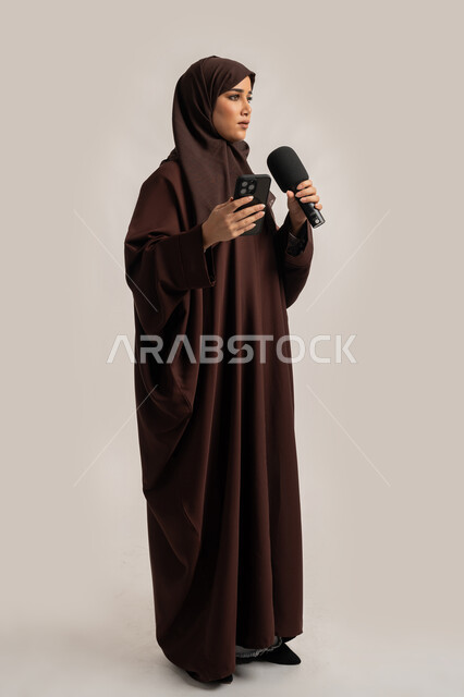 التواصل الفعال وتبادل الحوار والنقاش، إقامة ورش العمل والدورات التدريبية، إمرأة سعودية تقوم بالقراءة من الهاتف المحمول، فن الالقاء والخطابة، بورتريه لشابة عربية خليجية اماراتية محجبة ترتدي العباءة تمسك مكبر الصوت تلقي الخطابات، الجسم بالطول الكامل، خلفية بيضاء