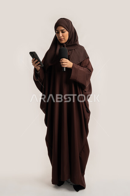 التواصل الفعال وتبادل الحوار والنقاش، إقامة ورش العمل والدورات التدريبية، إمرأة سعودية تقوم بالقراءة من الهاتف المحمول، فن الالقاء والخطابة، بورتريه لشابة عربية خليجية اماراتية محجبة ترتدي العباءة تمسك مكبر الصوت تلقي الخطابات، الجسم بالطول الكامل، خلفية بيضاء