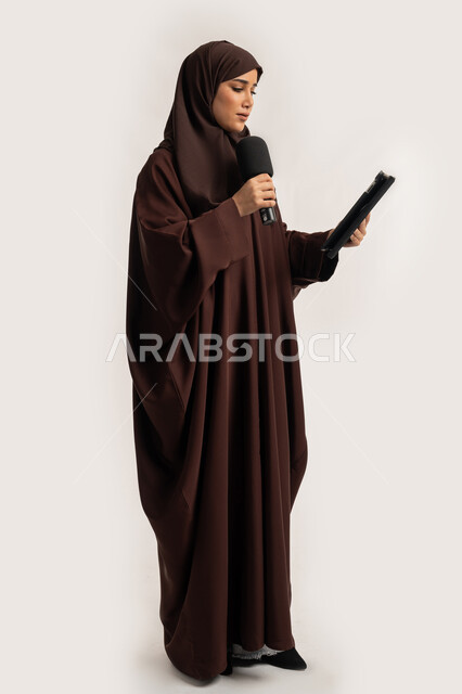 تبادل الحوار والتواصل الفعال، فن الالقاء والخطابة، إمرأة سعودية تقوم بالقراءة من التابلت، إقامة ورش العمل والدورات التدريبية، بورتريه لشابة عربية خليجية اماراتية محجبة ترتدي العباءة تمسك مكبر الصوت تقوم بإلقاء الخطابات بإيماءات الثقة، الجسم بالطول الكامل، خلفية بيضاء