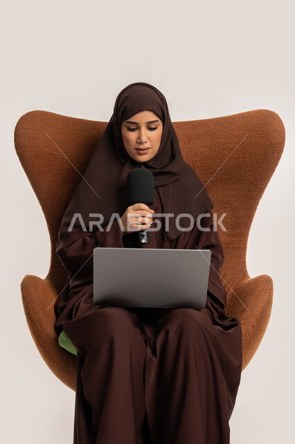 النقاش والتواصل الفعال، فن الالقاء والخطابة، إمرأة سعودية تجلس على الكرسي تقوم بالقراءة من الحاسب المحمول، إقامة ورش العمل والدورات التدريبية، بورتريه لشابة عربية خليجية اماراتية محجبة ترتدي العباءة تمسك مكبر الصوت تقوم بإلقاء الخطاب بإيماءات الثقة، خلفية بيضاء