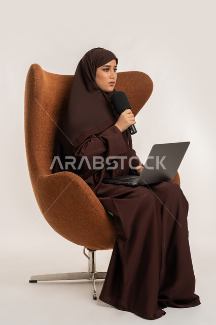 النقاش والتواصل الفعال، سيدة سعودية تجلس على الكرسي تقوم بالقراءة من الحاسب المحمول، إقامة ورش العمل والدورات التدريبية، بورتريه لشابة عربية خليجية اماراتية محجبة ترتدي العباءة تمسك مكبر الصوت تقوم بإلقاء الخطاب بإيماءات الثقة، فن التحدث والخطابة، خلفية بيضاء