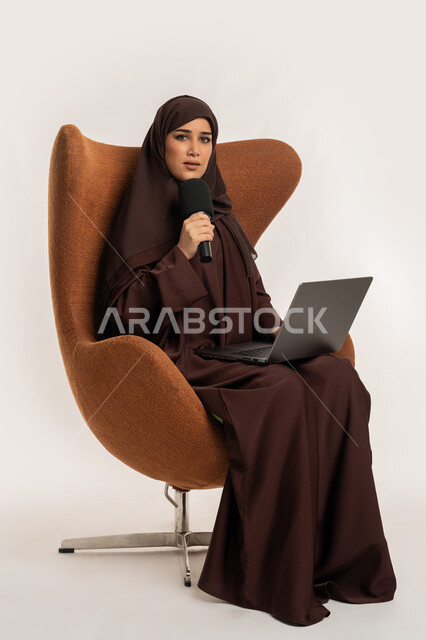 النقاش والتواصل الفعال، سيدة سعودية تجلس على الكرسي تقوم بالقراءة من الحاسب المحمول، إقامة ورش العمل والدورات التدريبية، بورتريه لشابة عربية خليجية اماراتية محجبة ترتدي العباءة تمسك مكبر الصوت تقوم بإلقاء الخطاب بإيماءات الثقة، فن التحدث والخطابة، خلفية بيضاء