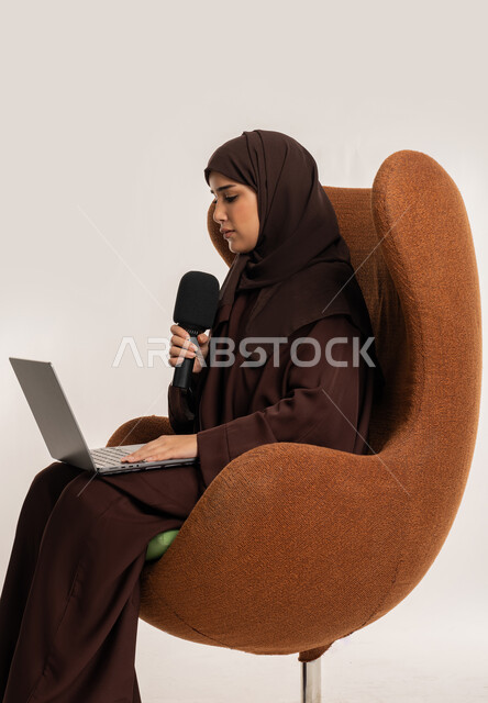 النقاش والتواصل الفعال، سيدة سعودية تجلس على الكرسي تقوم بالقراءة من الحاسب المحمول، إقامة ورش العمل والدورات التدريبية، بورتريه لشابة عربية خليجية اماراتية محجبة ترتدي العباءة تمسك مكبر الصوت تقوم بإلقاء الخطاب بإيماءات الثقة، فن التحدث والخطابة، خلفية بيضاء