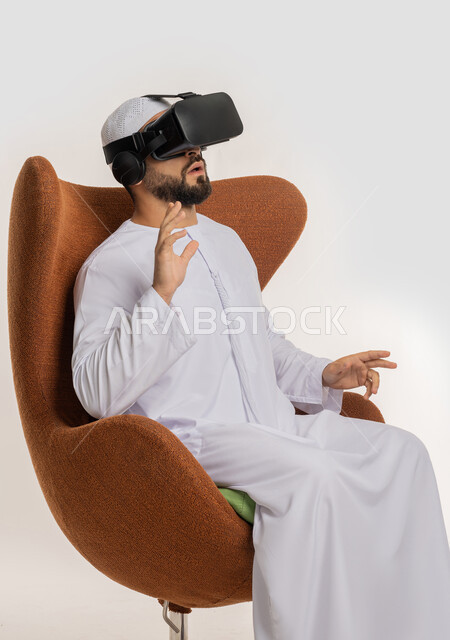 Fantasy world simulation and integration, side portrait of an Arab Gulf Emirati man wearing a kandura, ghutra and virtual reality glasses sitting on a chair extending his hands forward with expressions of repelling something and defending himself, using modern advanced technology and technology, white background
