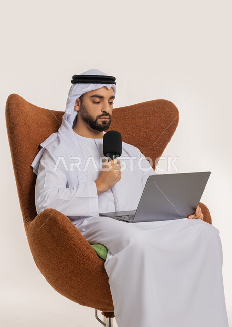 النقاش والتواصل الفعال، فن الالقاء والخطابة، دورة تدريبية اونلاين، اجراء مقابلة شخصية، بورتريه لشاب عربي خليجي اماراتي يرتدي الكندورة والغترة يمسك مكبر الصوت يجلس على الكرسي يقوم بالقراءة من الحاسب المحمول، إلقاء الخطاب بإيماءات الثقة بالنفس، خلفية بيضاء