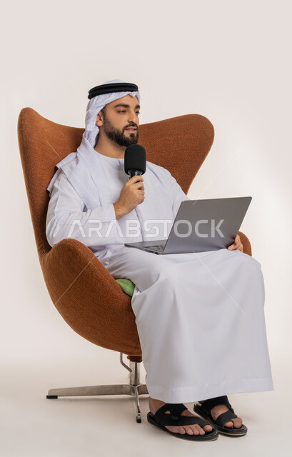 النقاش والتواصل الفعال، فن الالقاء والخطابة، دورة تدريبية اونلاين، اجراء مقابلة شخصية، بورتريه لشاب عربي خليجي اماراتي يرتدي الكندورة والغترة يمسك مكبر الصوت يجلس على الكرسي يقوم بالقراءة من الحاسب المحمول، إلقاء الخطاب بإيماءات الثقة بالنفس، خلفية بيضاء