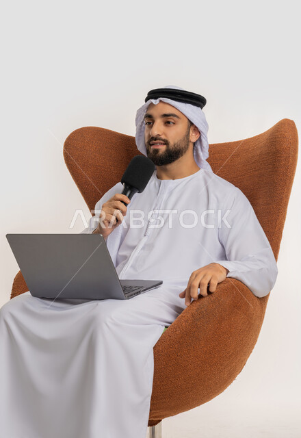 النقاش والتواصل الفعال، فن الالقاء والخطابة، دورة تدريبية اونلاين، اجراء مقابلة شخصية، بورتريه لشاب عربي خليجي اماراتي يرتدي الكندورة والغترة يمسك مكبر الصوت يجلس على الكرسي يقوم بالقراءة من الحاسب المحمول، إلقاء الخطاب بإيماءات الثقة بالنفس، خلفية بيضاء
