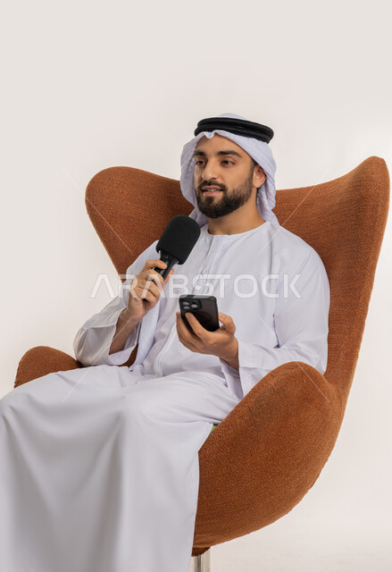 إقامة ورش العمل والدورات التدريبية، فن التحدث والخطابة، التواصل الفعال والنقاش، بورتريه لشاب عربي خليجي اماراتي يرتدي الكندورة والغترة يمسك مكبر الصوت يجلس على الكرسي تقوم بالقراءة من الهاتف المحمول، إلقاء الخطاب بإيماءات الثقة بالنفس، خلفية بيضاء