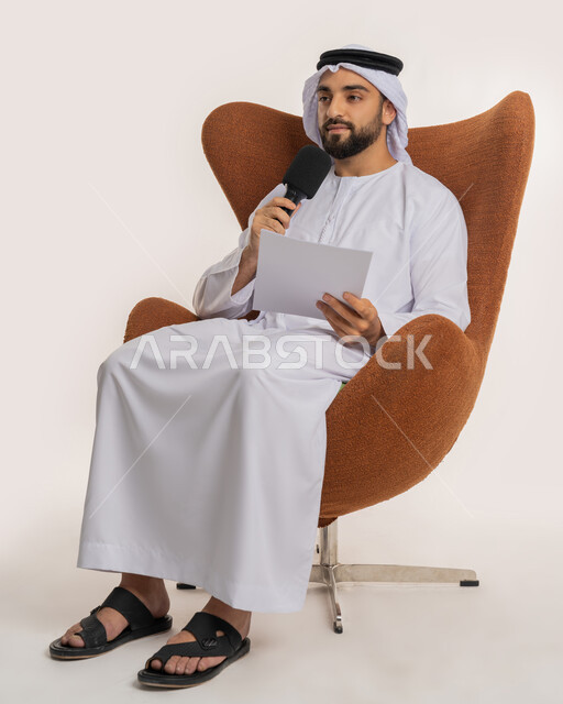 القاء الخطابات من الورقة بإيماءات الثقة بالنفس، تبادل الحوار والنقاش والتواصل الفعال، تقديم ورش العمل والدورات التدريبية، فن التحدث والخطابة، بورتريه لشاب عربي خليجي اماراتي يرتدي الكندورة والغترة يجلس على الكرسي يمسك مكبر الصوت، خلفية بيضاء