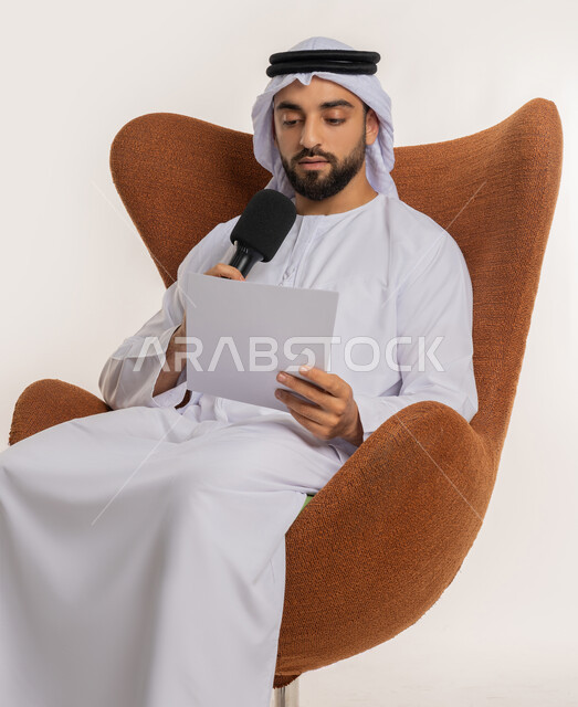 تقديم ورش العمل والدورات التدريبية، فن التحدث والخطابة، القاء الخطابات من الورقة بإيماءات الثقة بالنفس، التواصل الفعال وتبادل الحوار والنقاش، بورتريه لشاب عربي خليجي اماراتي يرتدي الكندورة والغترة يجلس على الكرسي يمسك مكبر الصوت، خلفية بيضاء