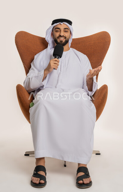 اتقان فن الالقاء والخطابة، مهارات التحدث والحوار، بورتريه لشاب عربي خليجي اماراتي يرتدي الكندورة والغترة يجلس على الكرسي يقوم بتقديم ورش العمل والدورات التدريبية باستخدام مكبر الصوت، ايماءات وتعابير الاندماج والتركيز، خلفيه بيضاء