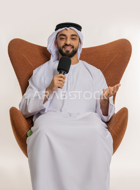 Mastering the art of public speaking and oratory, speaking and dialogue skills, portrait of a young Arab Gulf Emirati man wearing a kandura and ghutra sitting on a chair presenting workshops and training courses using a loudspeaker, gestures and expressions of integration and focus, white background