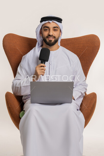 اجراء مقابلة شخصية، النقاش والتواصل الفعال، فن الالقاء والخطابة، دورة تدريبية اونلاين، بورتريه لشاب عربي خليجي اماراتي يرتدي الكندورة والغترة يمسك مكبر الصوت يجلس على الكرسي يقوم بالقراءة من الحاسب المحمول، إلقاء الخطاب بإيماءات الثقة بالنفس، خلفية بيضاء