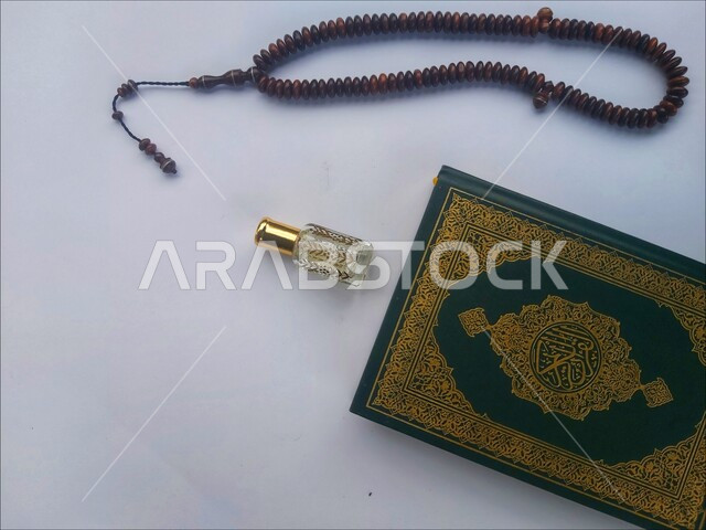 الاكثار من الاذكار في شهر رمضان المبارك، التعبد بتلاوة القران وحفظ وتفسير كلامه، صورة مقربة للمصحف الشريف مع سبحة وعطر، الجو الديني الروحاني, مفهوم التطيب والتعطر، الاجتهاد في الدعاء وطلب المغفرة, العبادة والتقرب إلى رب العالمين، خلفية بيضاء