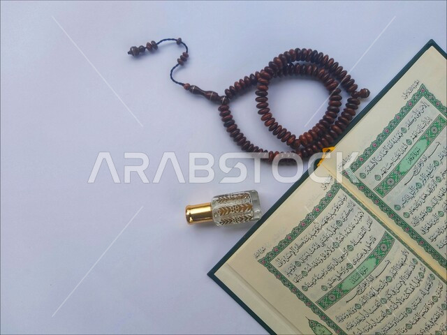 الاكثار من الاذكار في شهر رمضان المبارك، التعبد بتلاوة القران وحفظ وتفسير كلامه، صورة مقربة للمصحف الشريف مع سبحة وعطر، الجو الديني الروحاني, مفهوم التطيب والتعطر، الاجتهاد في الدعاء وطلب المغفرة, العبادة والتقرب إلى رب العالمين، خلفية بيضاء