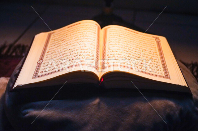 مفهوم العبادة والتقرب إلى الله في الأيام الفضيلة، التعبد بتلاوة القران وحفظ وتفسير كلامه في رمضان المبارك، صورة مقربة للمصحف الشريف مفتوح على وسادة مع سجادة الصلاة