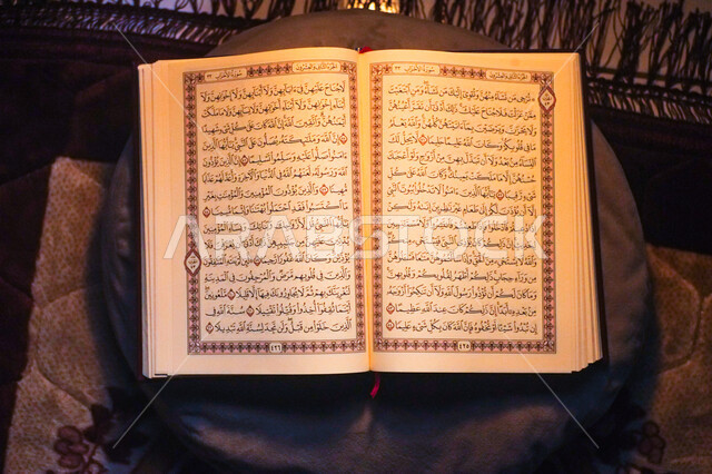 التعبد بتلاوة القران وحفظ وتفسير كلامه في رمضان المبارك، صورة من الاعلى للمصحف الشريف مفتوح على وسادة مع سجادة الصلاة، مفهوم العبادة والتقرب إلى الله في الأيام الفضيلة