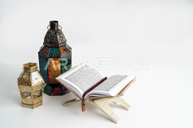 الأجواء الرمضانية الروحانية، التعبد بتلاوة القران وحفظ وتفسير كلامه، المصحف الشريف مفتوح على حامل خشبي مع سبحة وفانوسان معدنيان تقليديان، العبادة والتقرب إلى الله، ديكور وزينة شهر الخير، خلفية بيضاء