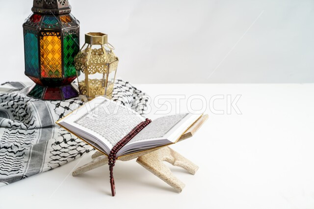 التعبد بتلاوة القران وحفظ وتفسير كلامه، الأجواء الرمضانية الروحانية، المصحف الشريف مفتوح على حامل خشبي مع سبحة وفانوسان معدنيان تقليديان، العبادة والتقرب إلى الله، ديكور وزينة شهر الخير، خلفية بيضاء