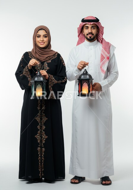 الجو الرمضاني الروحاني، الاستعداد لاستقبال شهر رمضان المبارك، بورتريه لرجل عربي خليجي سعودي يرتدي الشماغ والثوب التقليدي يقف برفقة زوجته يحملان فانوس معدني مزخرف، زينة الأعياد والمناسبات، الاحتفال بقدوم شهر الخير، الجسم بالطول الكامل، خلفية بيضاء