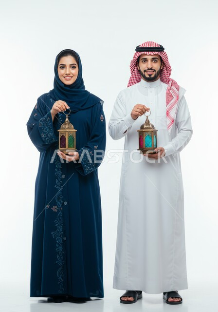 زينة الأعياد والمناسبات، الجو الرمضاني الروحاني، الاستعداد لاستقبال شهر رمضان المبارك، بورتريه لرجل عربي خليجي سعودي يرتدي الشماغ والثوب التقليدي يقف برفقة زوجته يحملان فانوس معدني مزخرف، الاحتفال بقدوم شهر الخير، الجسم بالطول الكامل، خلفية بيضاء