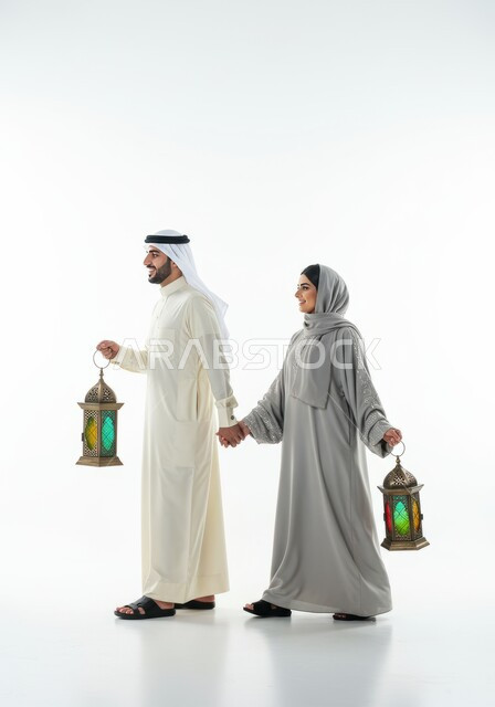 الجو الرمضاني الروحاني، الاستعداد لاستقبال شهر رمضان المبارك، بورتريه من الجانب لرجل عربي خليجي سعودي يرتدي الغترة والثوب التقليدي يمشي برفقة زوجته يحملان فانوس معدني مزخرف، زينة الأعياد والمناسبات، الاحتفال بقدوم شهر الخير، الجسم بالطول الكامل، خلفية بيضاء 