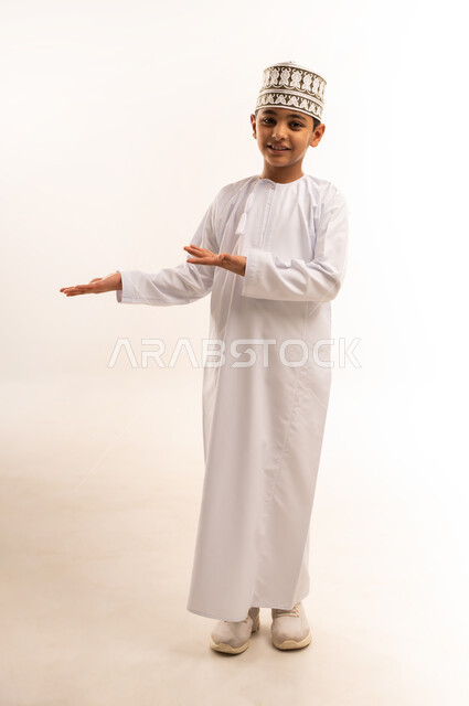 رفع وحمل العناصر، تقديم وعرض عنصر ما، استخدام حاسة اللمس لتحريك العناصر الهولوجراميه، بورتريه لولد عربي خليجي عماني يرتدي الدشداشة والكمة ينظر الى الكاميرا يرفع يده بايماءات حمل شيء ويقوم بالاشارة اليه، صورة الجسم بالطول الكامل، خلفية بيضاء
