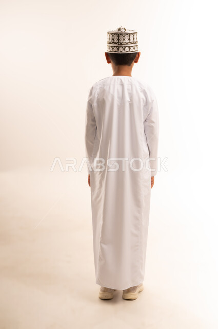 مفهوم الثقه بالنفس، الاهتمام بالاناقه بالمظهر الخارجي، بورتريه من الخلف لولد عربي خليجي عماني يرتدي الدشداشة والكمة يقف باستقامة، صورة الجسم بالطول الكامل، خلفية بيضاء