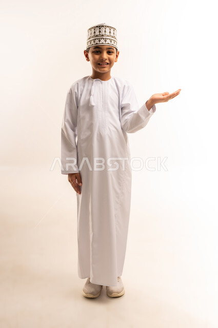 تقديم وعرض عنصر ما، رفع وحمل العناصر، استخدام حاسة اللمس لتحريك العناصر الهولوجراميه، بورتريه لولد عربي خليجي عماني يرتدي الدشداشة والكمة ينظر الى الكاميرا يرفع يده بايماءات حمل شيء، صورة الجسم بالطول الكامل، خلفية بيضاء