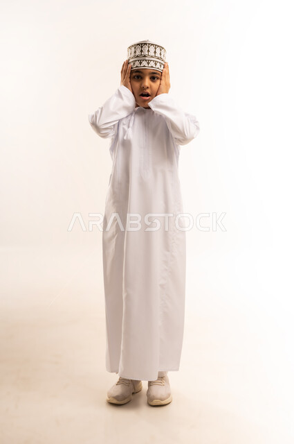 تعابير الاضطراب والانزعاج من الصوت العالي, الحاجة إلى الهدوء والسكون، بورتريه لولد عربي خليجي عماني يرتدي الدشداشة والكمة يقوم بإغلاق أذنيه بأصابعه للتخفيف من الضجيج المحيط به، الطول الكامل للجسم، خلفية بيضاء