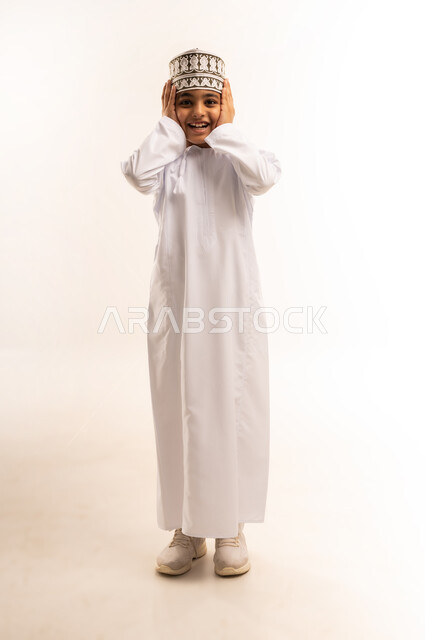 إيماءات الاضطراب والانزعاج من الصوت العالي, الحاجة إلى الهدوء والسكون، بورتريه لولد عربي خليجي عماني يرتدي الدشداشة والكمة يقوم بإغلاق أذنيه بأصابعه للتخفيف من الضجيج المحيط به، الطول الكامل للجسم، خلفية بيضاء