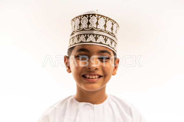 الاهتمام بالمظهر الخارجي, بورتريه مقرب لولد عربي خليجي عماني يرتدي الدشداشة و الكمة ينظر إلى الكاميرا بإيماءات السرور والسعادة، مفهوم الاناقة والوسامة، خلفية بيضاء