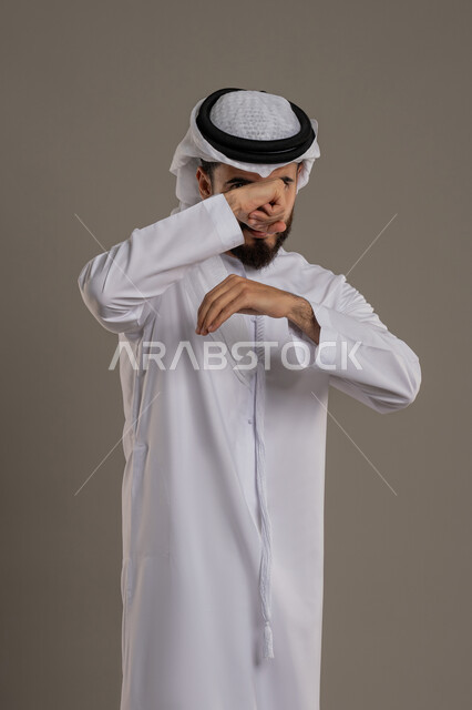 Closing the hand and preparing to attack and confront, professional boxing, trying to defend oneself, the concept of strength and masculinity, portrait of an Arab Gulf Emirati man wearing a kandura and a ghutra looking at the camera with gestures of seriousness and anger, gray background