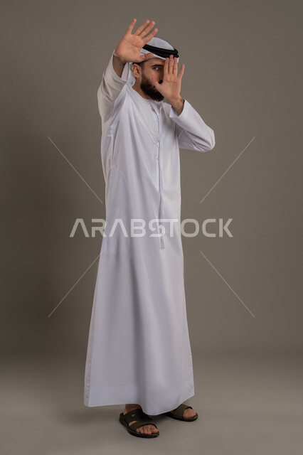 الرفض وعدم الخضوع، النهي عن التقدم وأهمية ترك مسافة أمان، طلب التوقف عن فعل شيء ما، الأمر بالوقوف وعدم التمادي، بورتريه لرجل عربي خليجي اماراتي يرتدي الكندورة والغترة يرفع كفه للأعلى، الجسم بالطول الكامل، خلفية رمادي