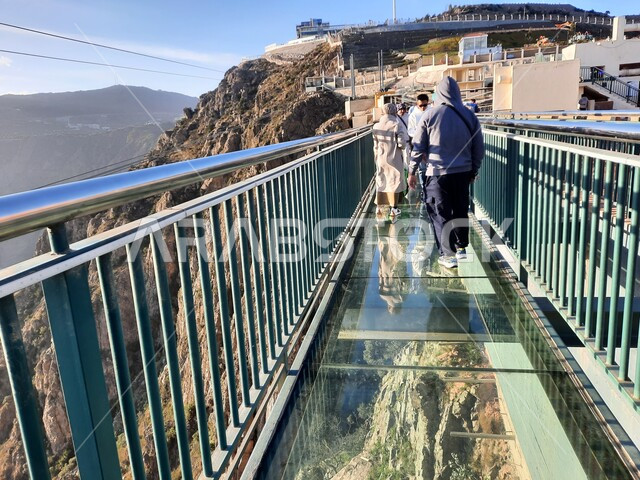 منظر طبيعي متميز، التشكيل والتكوين الصخري للجبل في المملكة العربية السعودية، صورة من الخلف للسائحين على الجسر الزجاجي في حديقة الأمير حسام في محافظة الباحة، المنتزهات والحدائق العامة، معلم سياحي مشهور، مكان جذب واستقطاب السائحين
