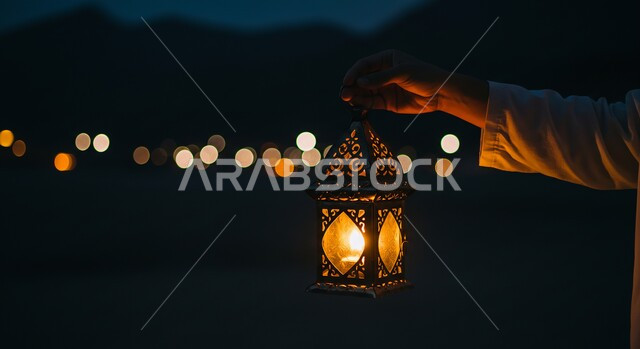 تحف واكسسوارات وزينة رمضان المبارك، صورة مقربة من الجانب لرجل عربي خليجي سعودي يرتدي الثوب التقليدي يحمل بيده فانوس معدني مزخرف ومضيئ، استقبال الأجواء الرمضانية الروحانية في المملكة العربية السعودية، المناسبات الدينية والأعياد الإسلامية