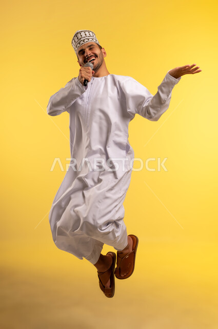 تقديم العروض الصوتية، تسجيل مقطع صوتي غنائي، بورتريه لرجل عربي خليجي عماني يرتدي الدشداشة والكمة يقفز عاليا يمسك بيده المايكروفون يغني بإيماءات الحماس والسرور، ممارسة موهبة الغناء، تعابير الاندماج والتفاعل مع الموسيقا، الجسم بالطول الكامل، خلفية صفراء