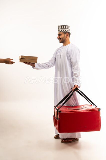 ضمان سلامة الطرود المرسلة، بورتريه من الجانب لشاب عربي خليجي عماني يرتدي الدشداشة والكمة يحمل حقيبة حمراء يقوم بتسليم طرد إلى شخص اخر، عملية الشحن والتوصيل الموثوقة، أداء العمل بدقة واتقان، التسوق وشراء الحاجيات عبر الانترنت، الجسم بالطول الكامل، خلفية بيضاء