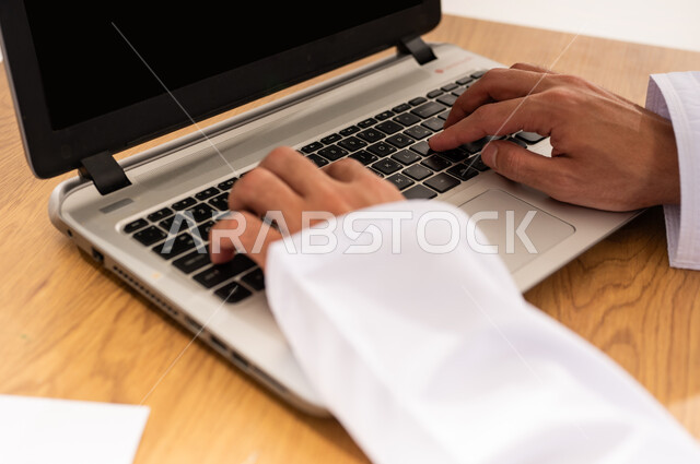 Developing business strategy and growth plan, using advanced modern technology, company profit and loss statements, monitoring the economy and financial information, close-up portrait of an Arab Gulf Omani man wearing a kimmah and a dishdasha sitting at a wooden table working on a laptop, white background