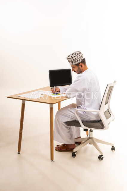 مهنة ووظيفه شبابية عمانية, التحقق والتدقيق في المعلومات, دمج التقنية الحديثة المتطورة في الحياة العملية, بورتريه لرجل عربي خليجي عماني يرتدي الكمه و الدشداشة يجلس على كرسي أمام طاولة خشبية يقوم بتوقيع التقرير الشهري, خلفية بيضاء