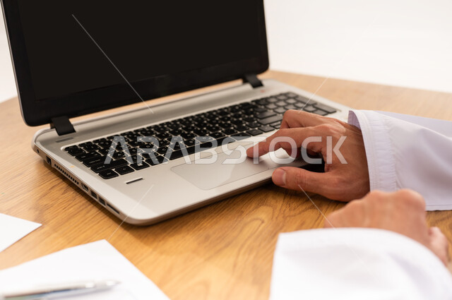 استخدام تقنية حديثة متطورة, بيانات خسائر وأرباح الشركة, تطوير استراتيجية العمل وخطة النمو، مراقبة الاقتصاد والمعلومات المالية، بورتريه مقرب لرجل عربي خليجي عماني يرتدي الكمه و الدشداشة يجلس على طاولة خشبية يعمل على جهاز الحاسوب المحمول, خلفية بيضاء