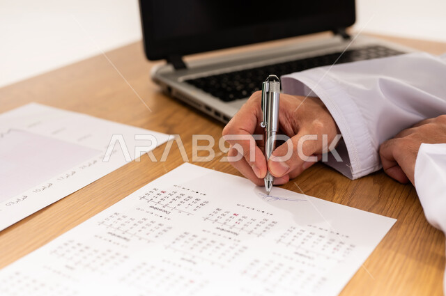 دمج التقنية الحديثة المتطورة في الحياة العملية,بورتريه مقرب لرجل عربي خليجي عماني يرتدي الزي التقليدي يجلس أمام طاولة خشبية يقوم بتوقيع التقرير الشهري, التحقق والتدقيق في المعلومات, مهنة ووظيفه شبابية عمانية, خلفية بيضاء