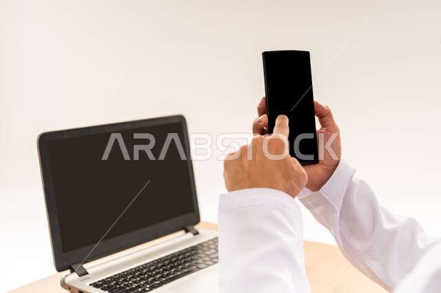Blank black screen view on laptop, close up portrait of an Omani Gulf Arab man in traditional dress pressing index finger on mobile screen, digital marketing and advertising promotions, integrating modern advanced technology with business life, white background